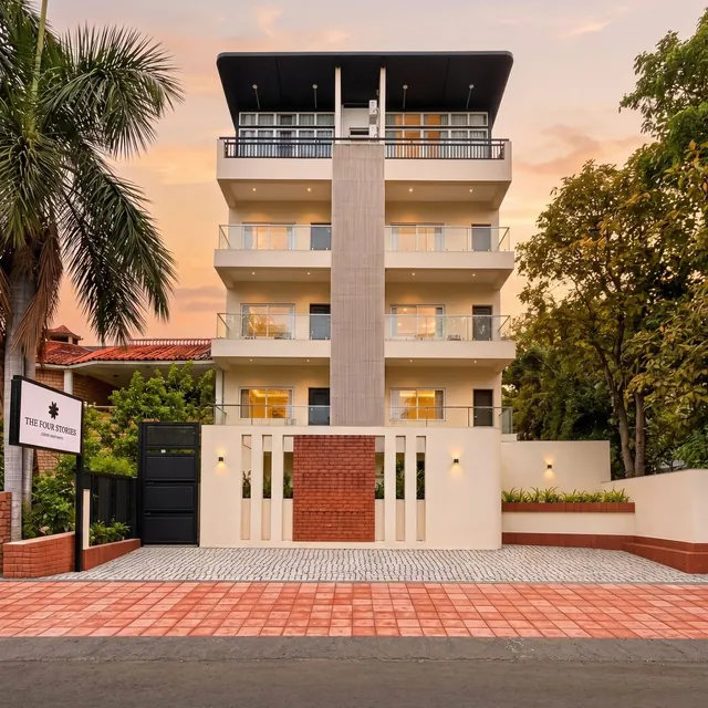 The Four Stories hotel in Udaipur at dusk: a cream four-storey facade with glass balconies, palms and the hotel sign by the gate